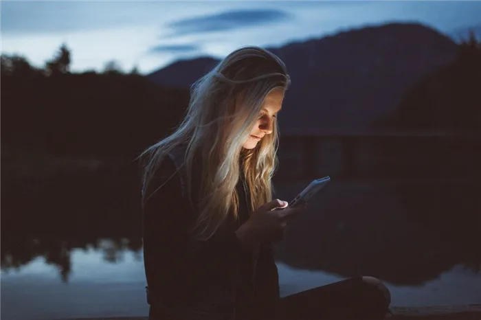 Девушка смотрит на экран смартфона, стоя на фоне озера