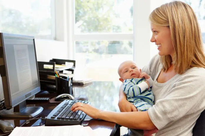девушка с малышом на руках работает за компьютером