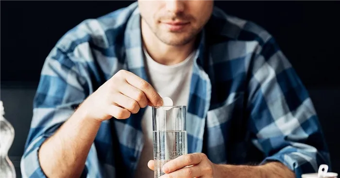 мужчина растворяет в стакане с водой таблетку от похмелья