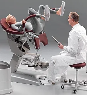Женщина сидит на гинекологическом кресле с подтянутыи к животу ногами